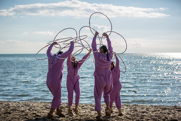 Four ring dancers wearing magenta jump suits at the beach in a circle formation