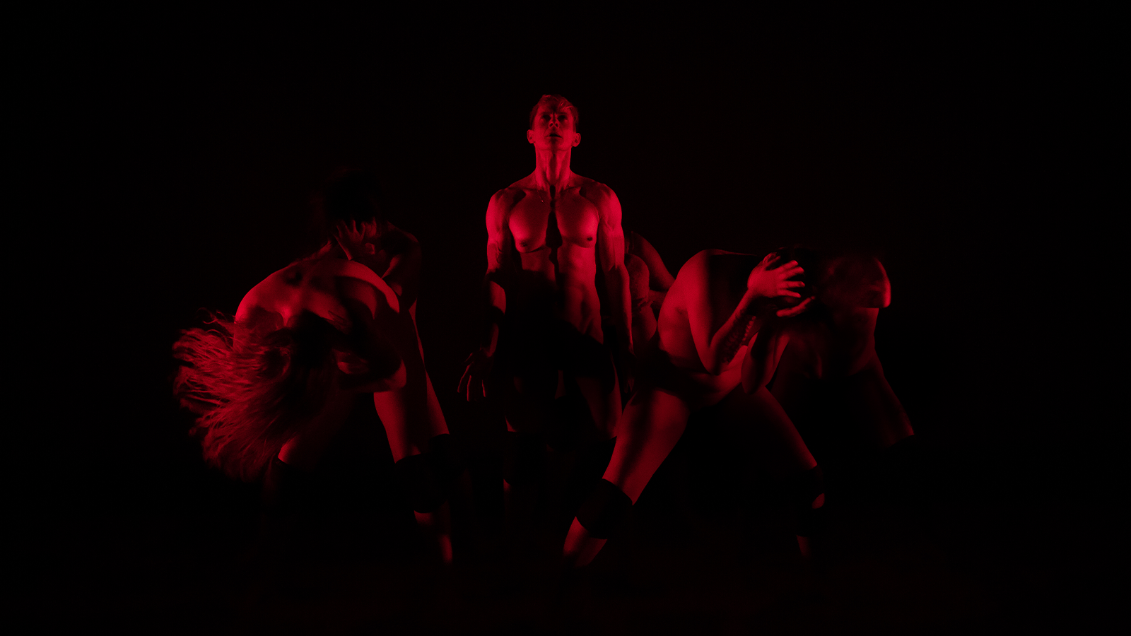 Dancers on stage in a dark space under red neon lights 