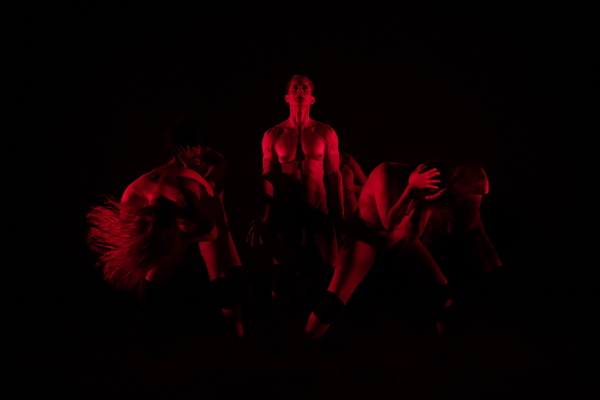 Dancers on stage in a dark space under red neon lights