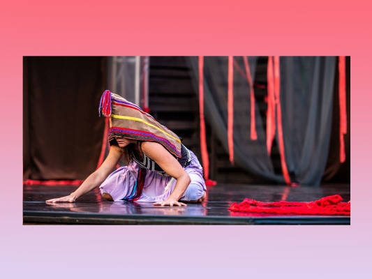 female dancer crouched down on the stage floor wearing light purple skirt and black top with head piece covering face