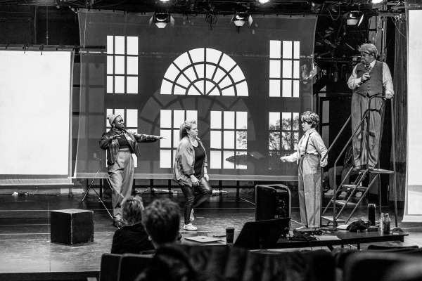 Four performers on stage in front of a large window backdrop.