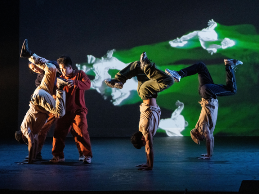 Two dancers standing on their hands; a third being helped into this position by two others.