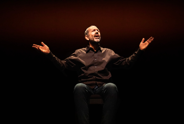 A man in black a button-up sits and holds his arms to their air.