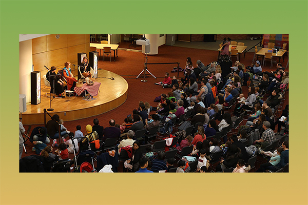 3 people on stage with a crowd of people listening to them